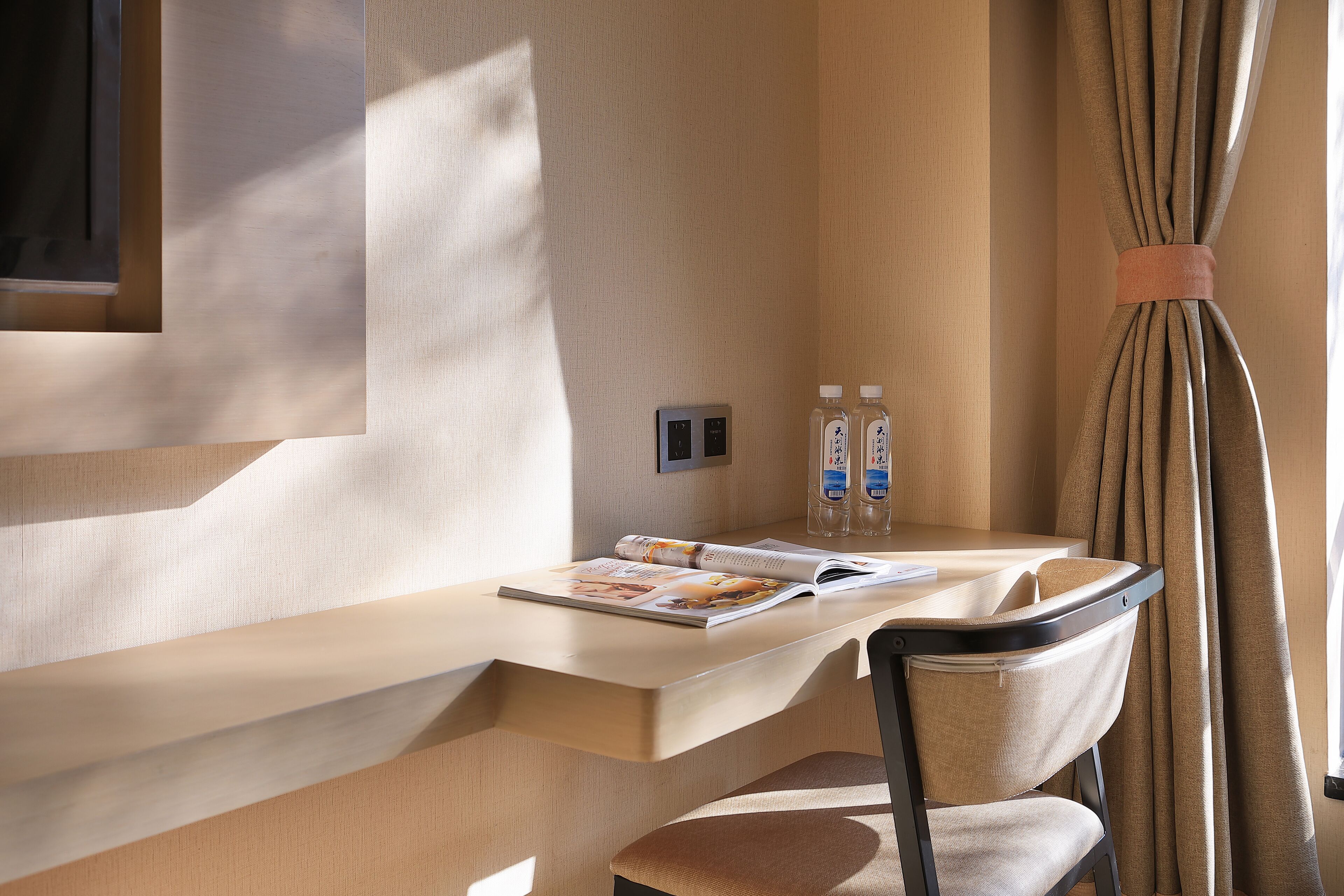A modern room with a wooden desk, a chair, a magazine, and two bottles of water.