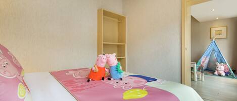 Un dormitorio infantil con una cama, un edredón rosa y blanco, y dos peluches sobre la cama.