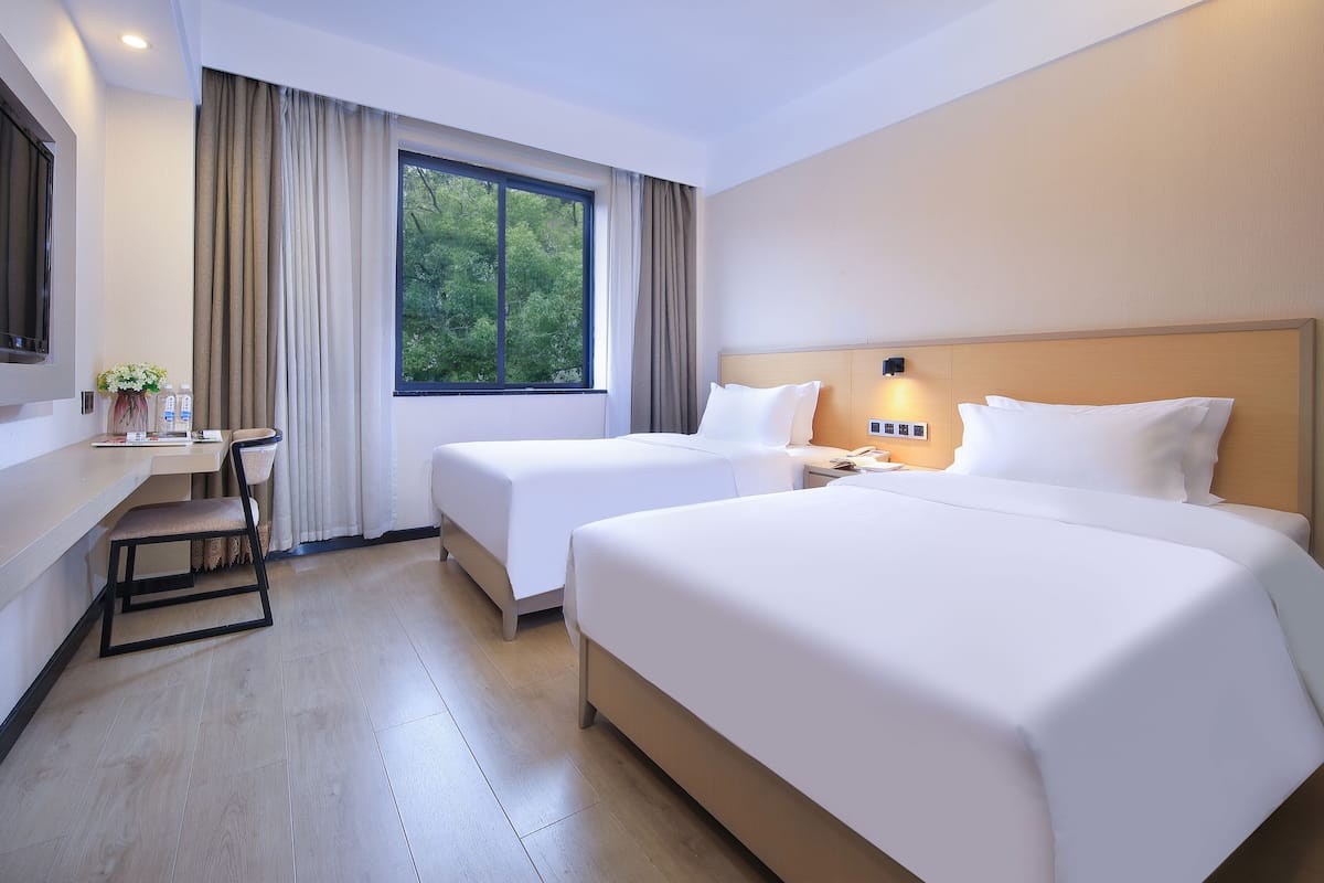 A hotel room with two beds, a desk, and a window with curtains.