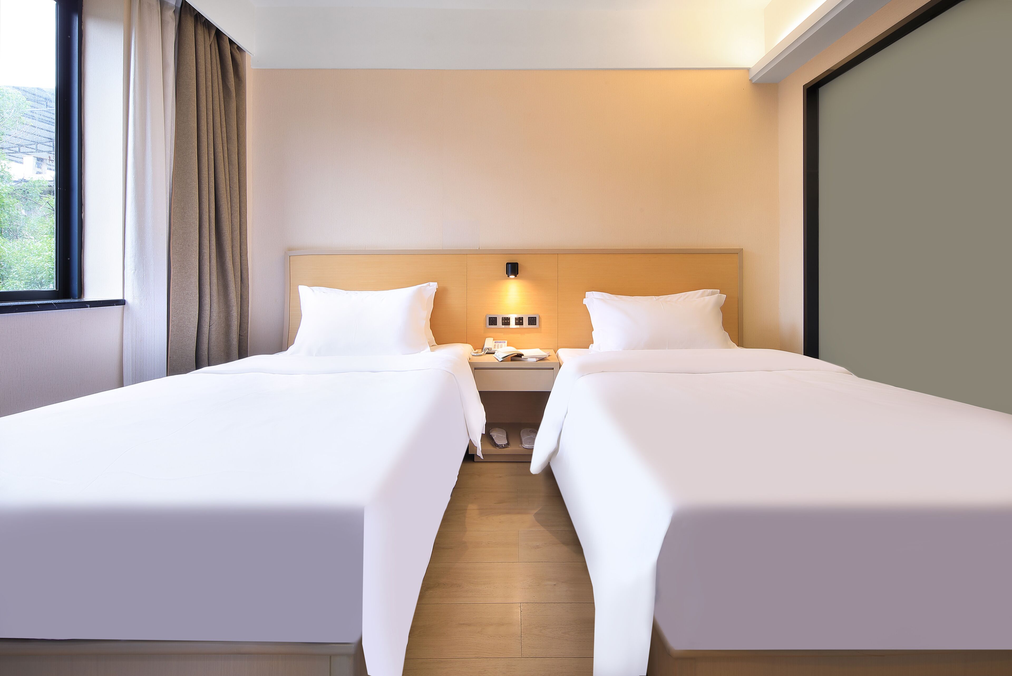 A hotel room with two beds, a nightstand, a lamp, and a window with curtains.
