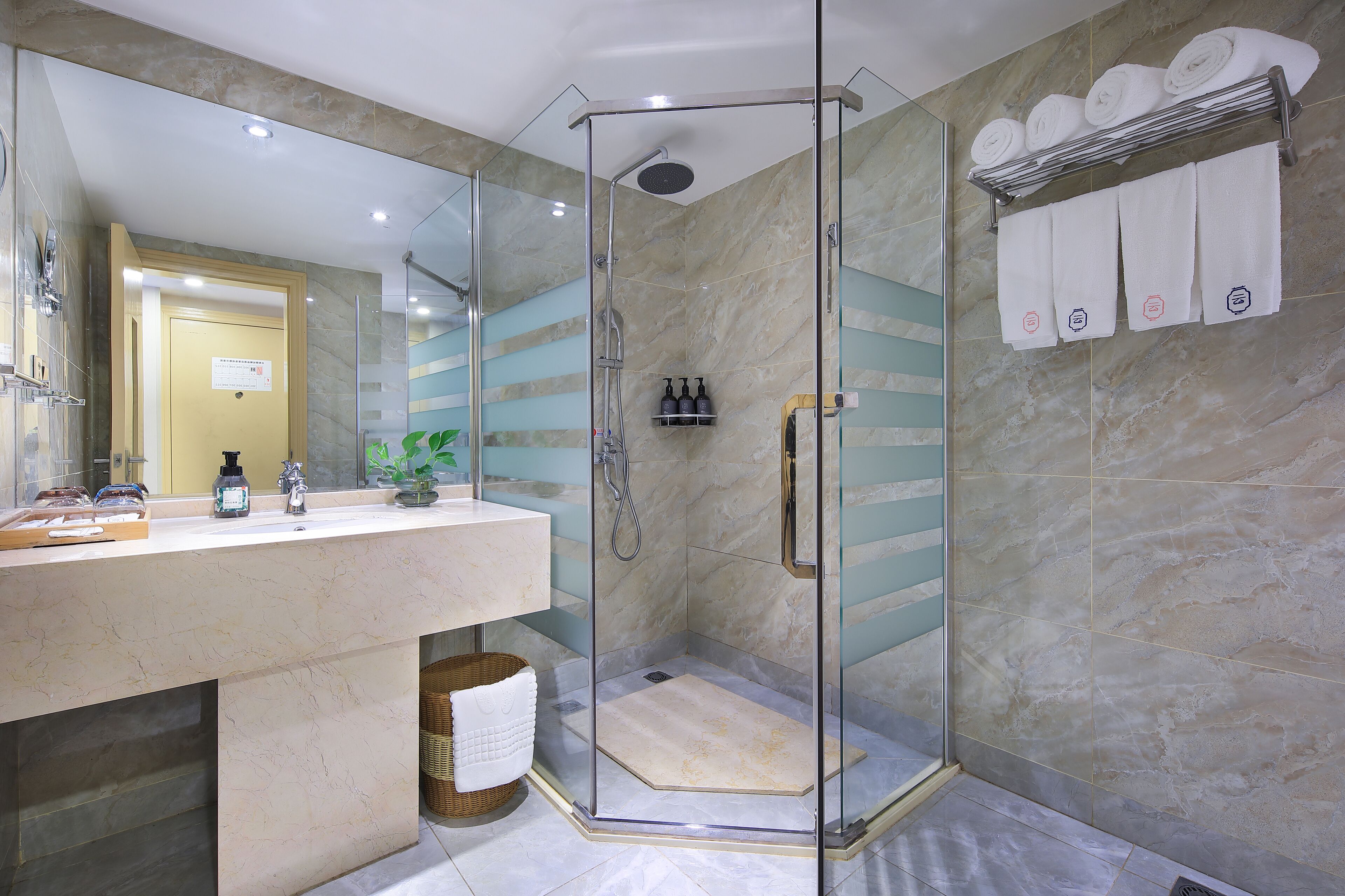 Une salle de bain moderne avec une douche à parois de verre, un mur recouvert de carreaux de marbre, un meuble-lavabo avec des articles de toilette et des serviettes soigneusement pliées sur un porte-serviettes.