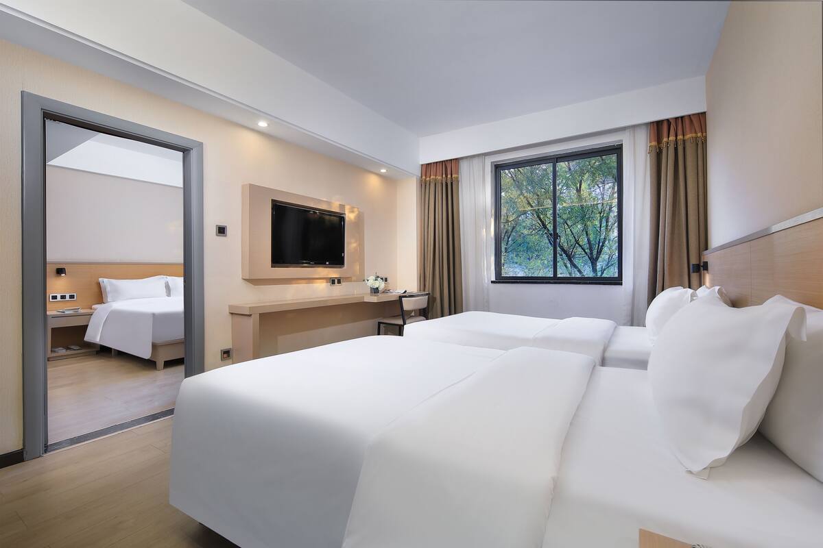 A hotel room with two beds, a TV, a desk, and a window with curtains.