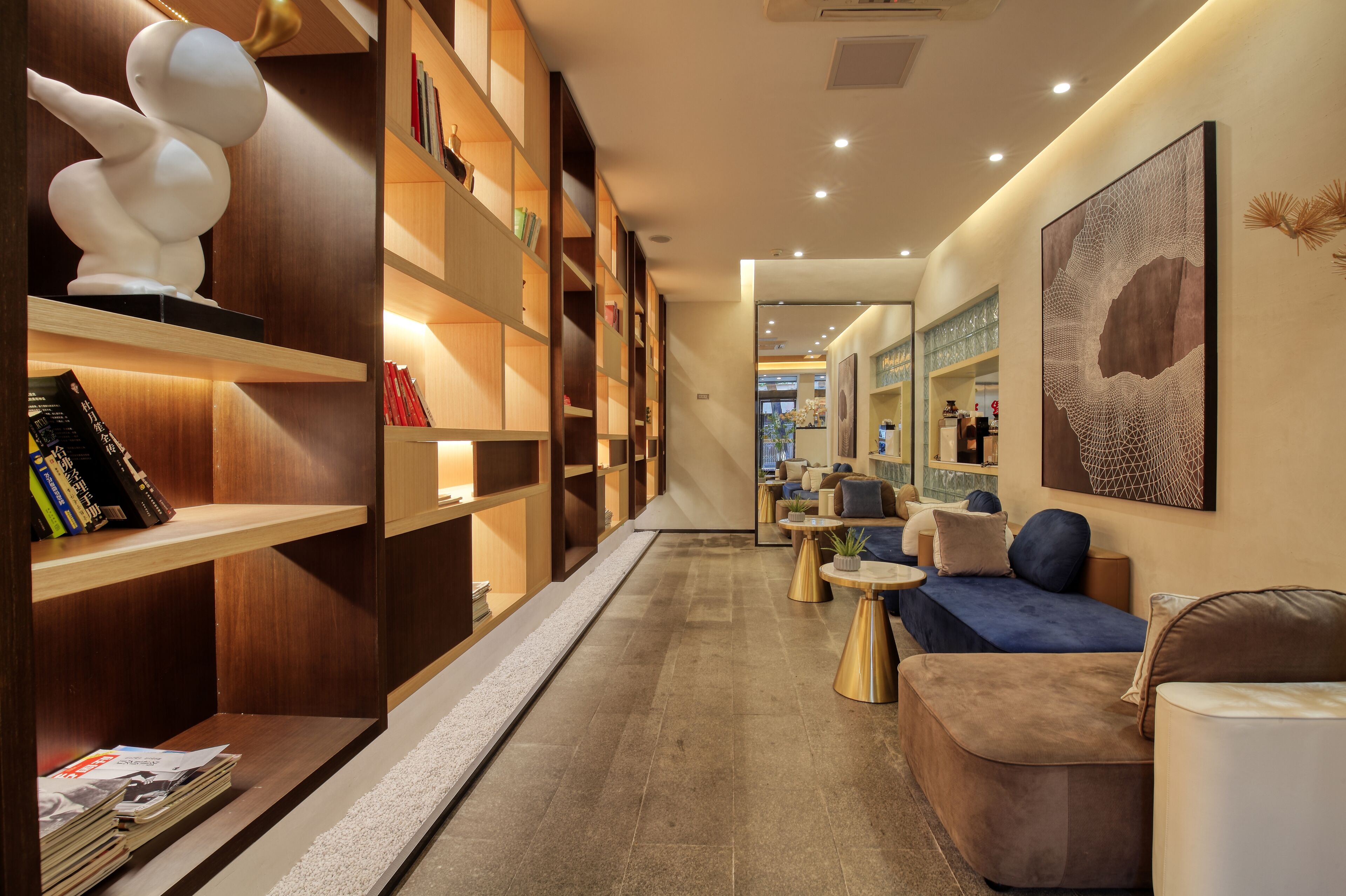 A modern library with bookshelves, a sculpture, and a seating area with sofas and tables.