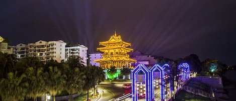 A brightly lit pagoda-style building with a traditional architectural design, surrounded by modern buildings and a well-lit street at night.