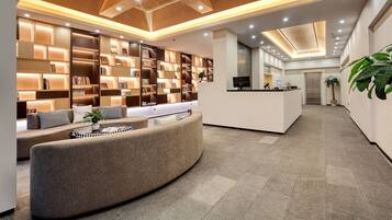 A modern lobby with a curved sofa, a reception desk, and a wall of bookshelves.