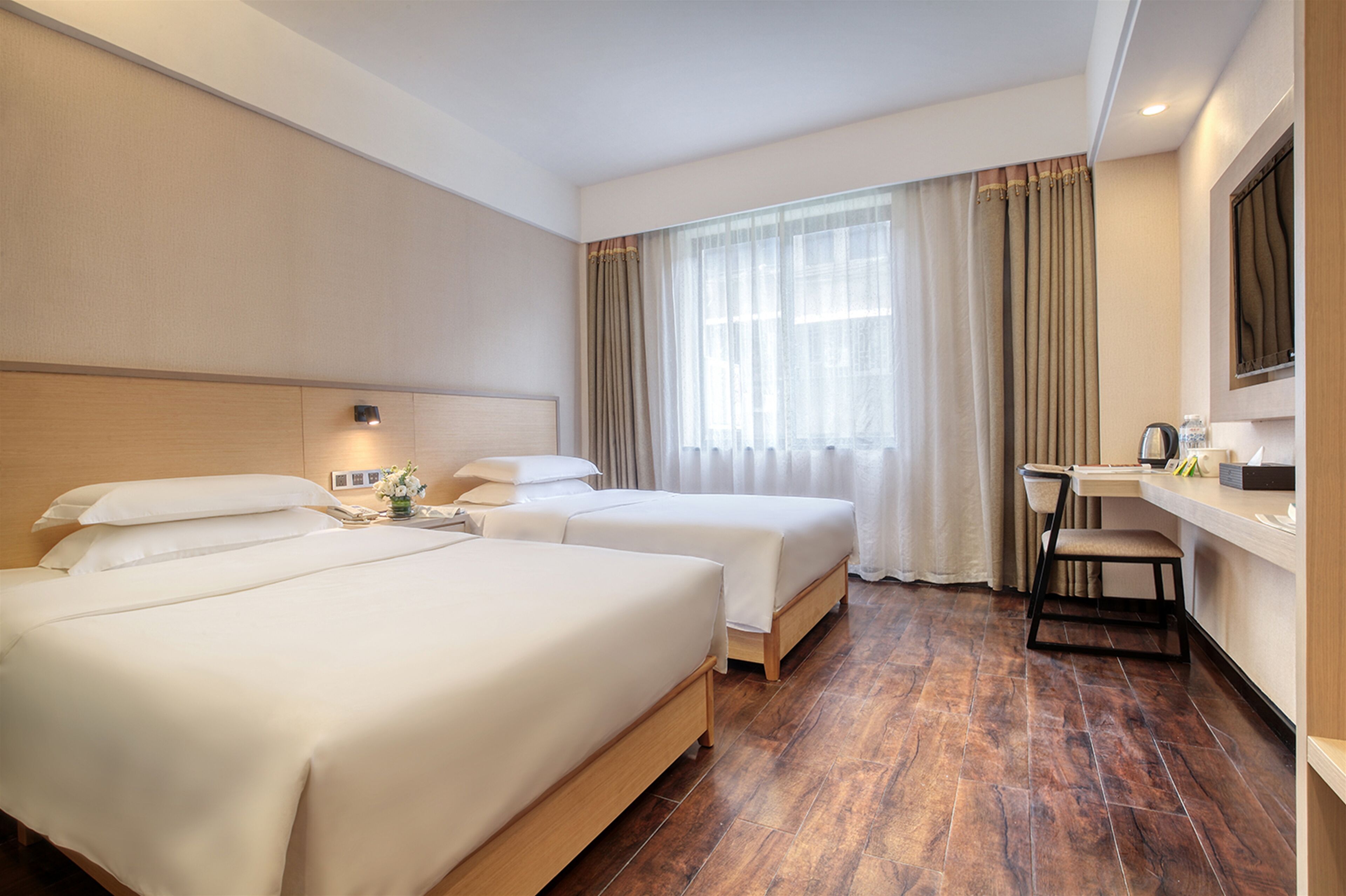 A hotel room with two beds, a desk, a chair, and a large window with curtains.