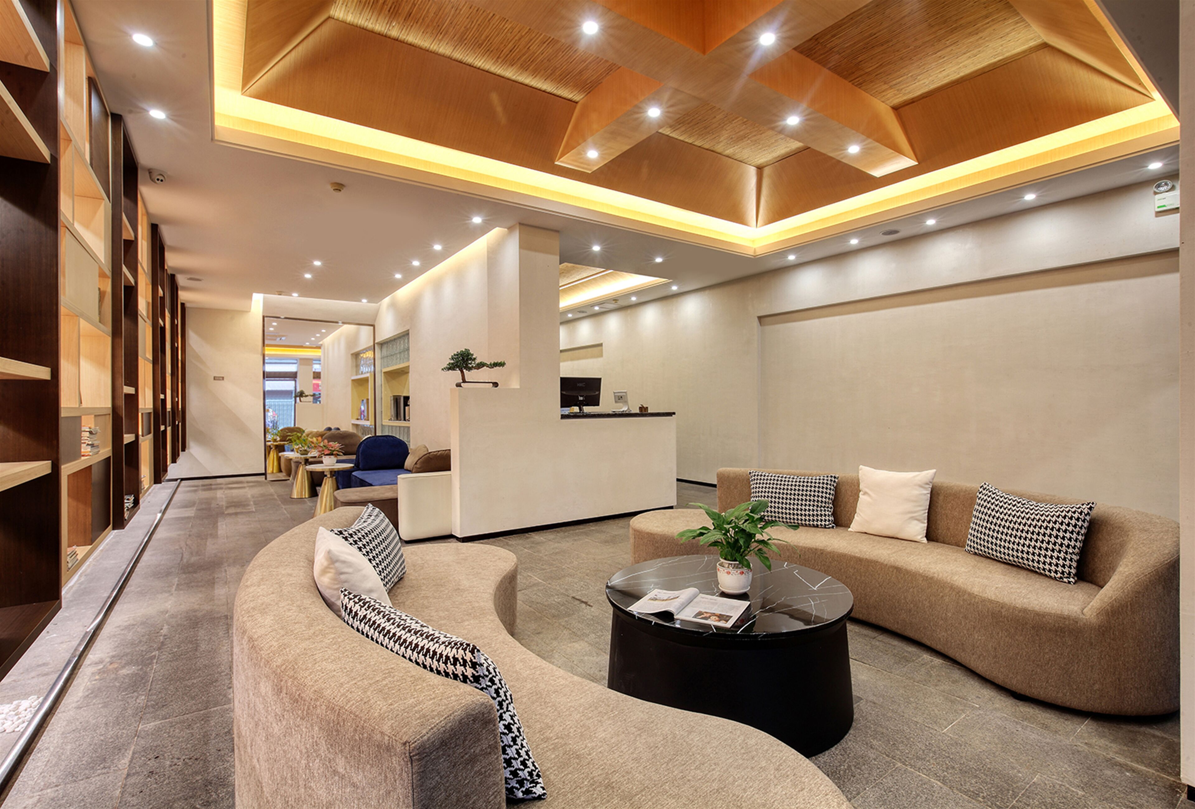 A modern hotel lobby with a curved sofa, a round coffee table, and a reception desk.