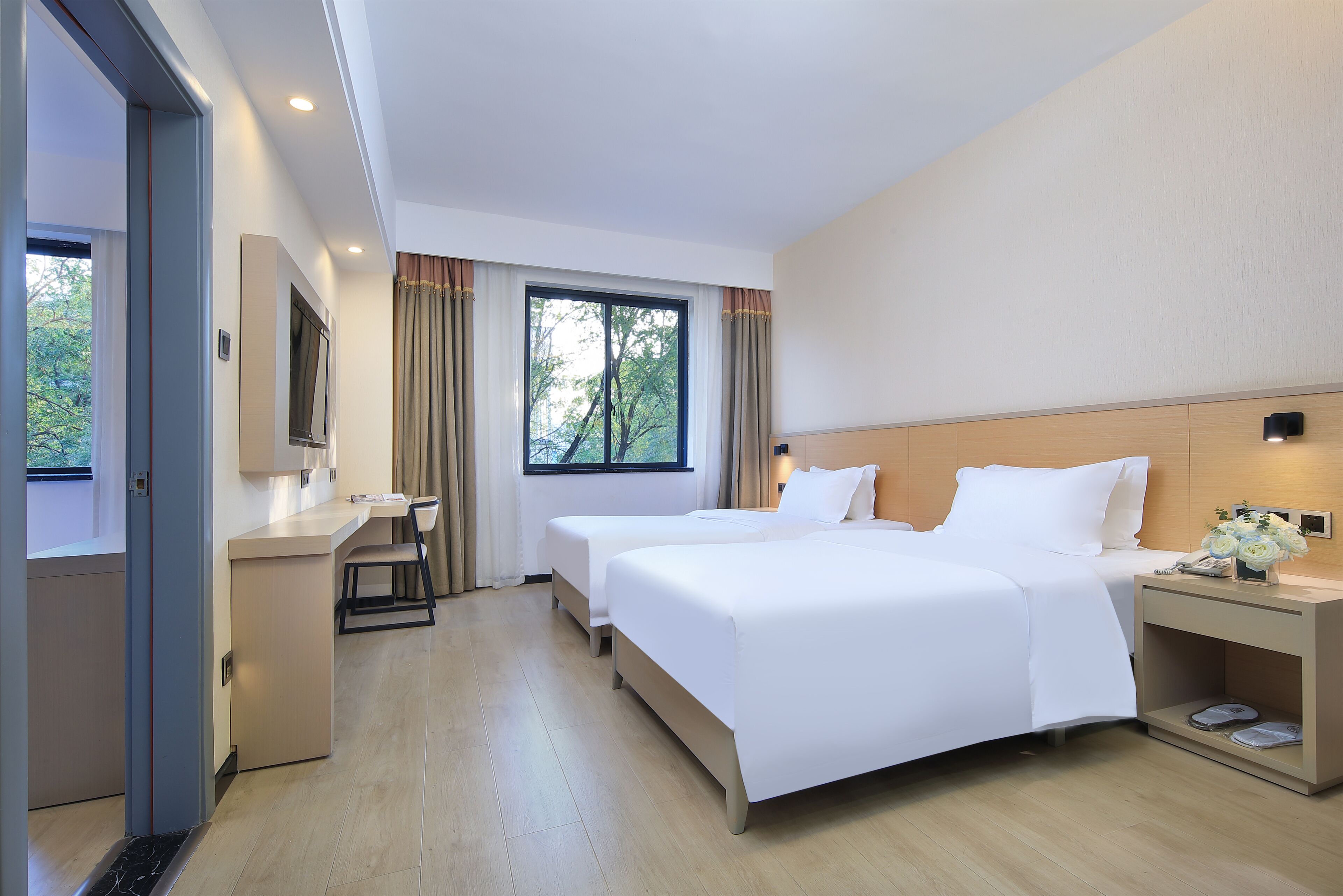 Ein Hotelzimmer mit zwei Betten, einem Schreibtisch, einem Spiegel und einem Fenster mit Vorhängen.