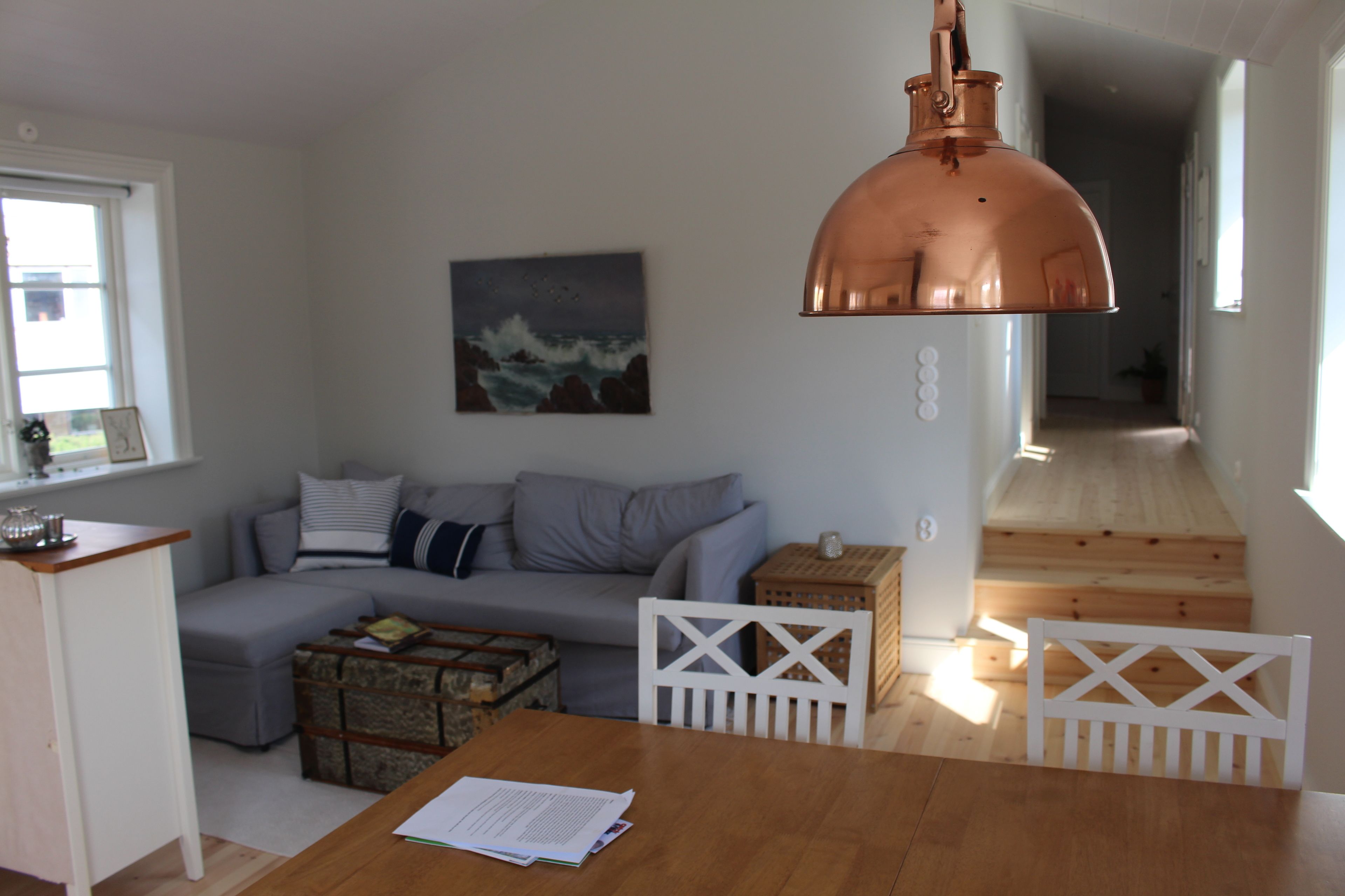 A modern living room with a grey sofa, a wooden coffee table, a white chair, and a copper pendant light.