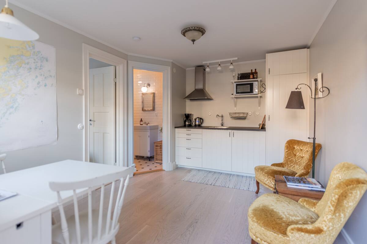 Une cuisine moderne avec des meubles blancs, un four à micro-ondes et un évier. On y trouve également un coin repas avec une table et des chaises blanches.