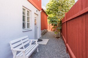 A narrow outdoor area with a white bench, a red wooden fence, and a white building with a window and door. - Vaxholm Harbour Bed and Experiences (Vaxholm)