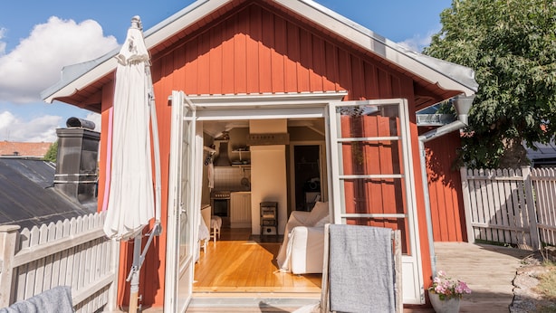 Een rood houten gebouw met een houten terras en een witte parasol.
