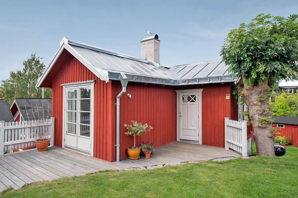 Une maison en bois rouge avec une porte blanche, une grande fenêtre et une cheminée.