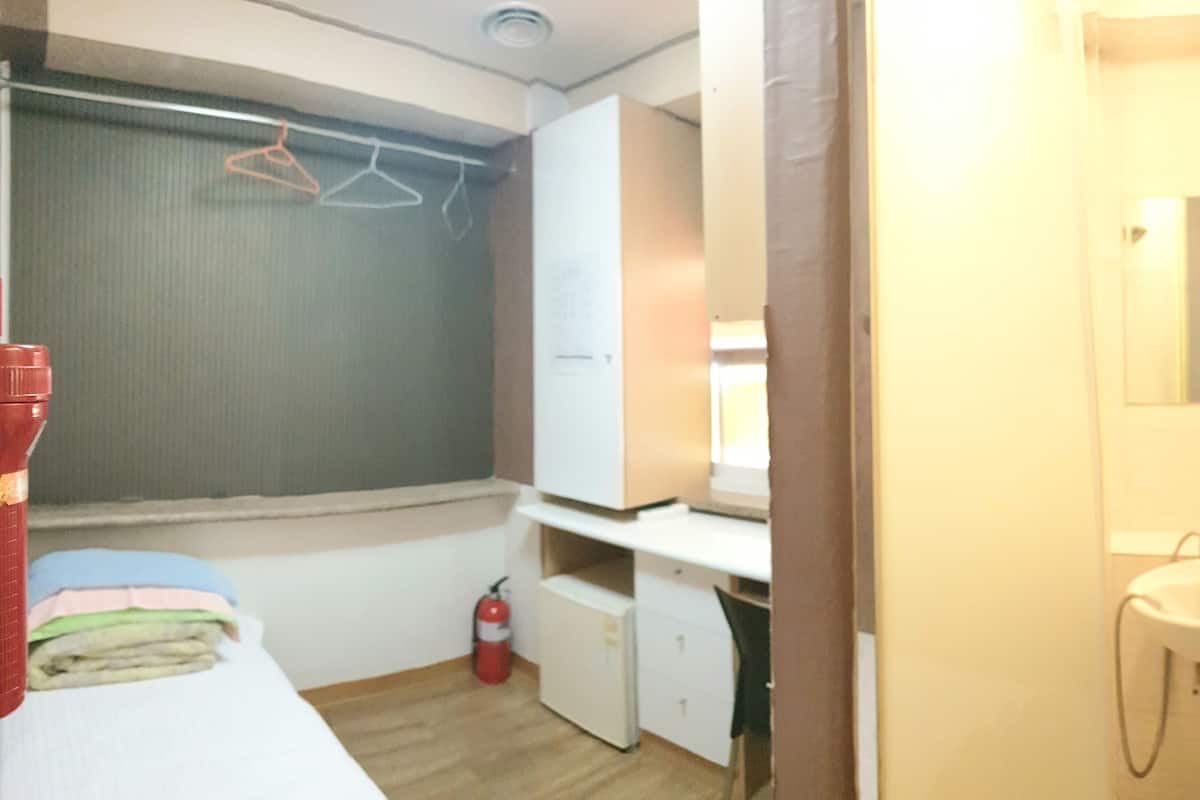 A compact room with a bed, a small desk, a wardrobe, and a bathroom with a sink and mirror.