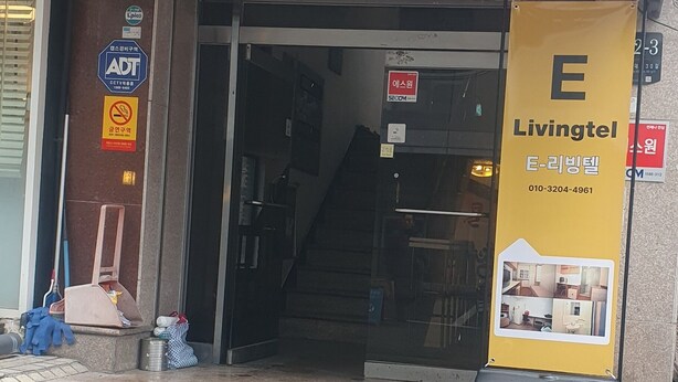 L’entrée d’un immeuble, avec une enseigne indiquant « Livingtel » et un escalier menant à l’étage.