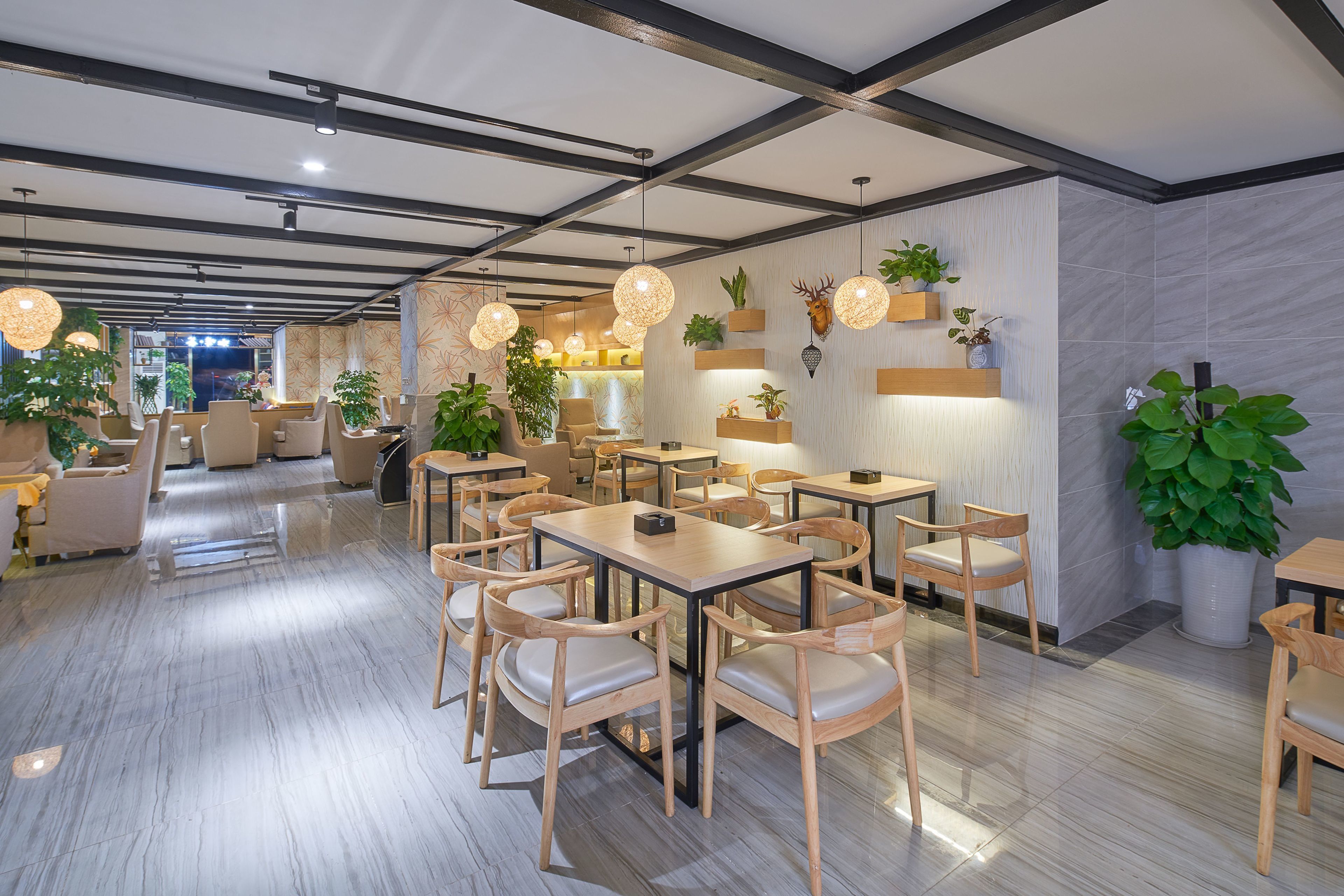 A modern restaurant with wooden tables and chairs, hanging pendant lights, and potted plants.