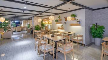 A modern restaurant with wooden tables and chairs, hanging pendant lights, and potted plants.