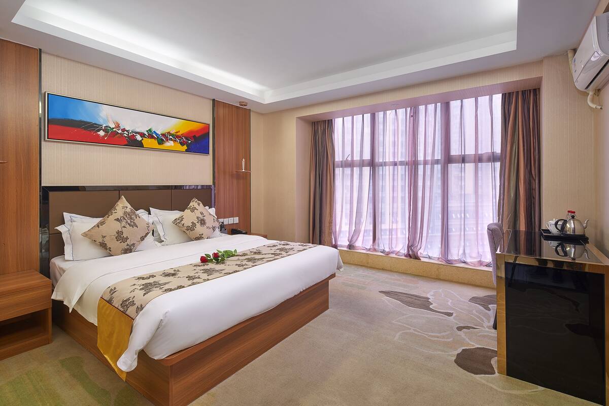 A hotel room with a large bed, a desk, a TV, and a window with curtains.