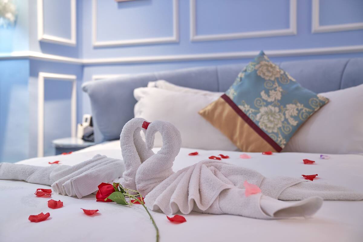 A neatly made bed with towels arranged in a swan shape, a single rose, and scattered rose petals.