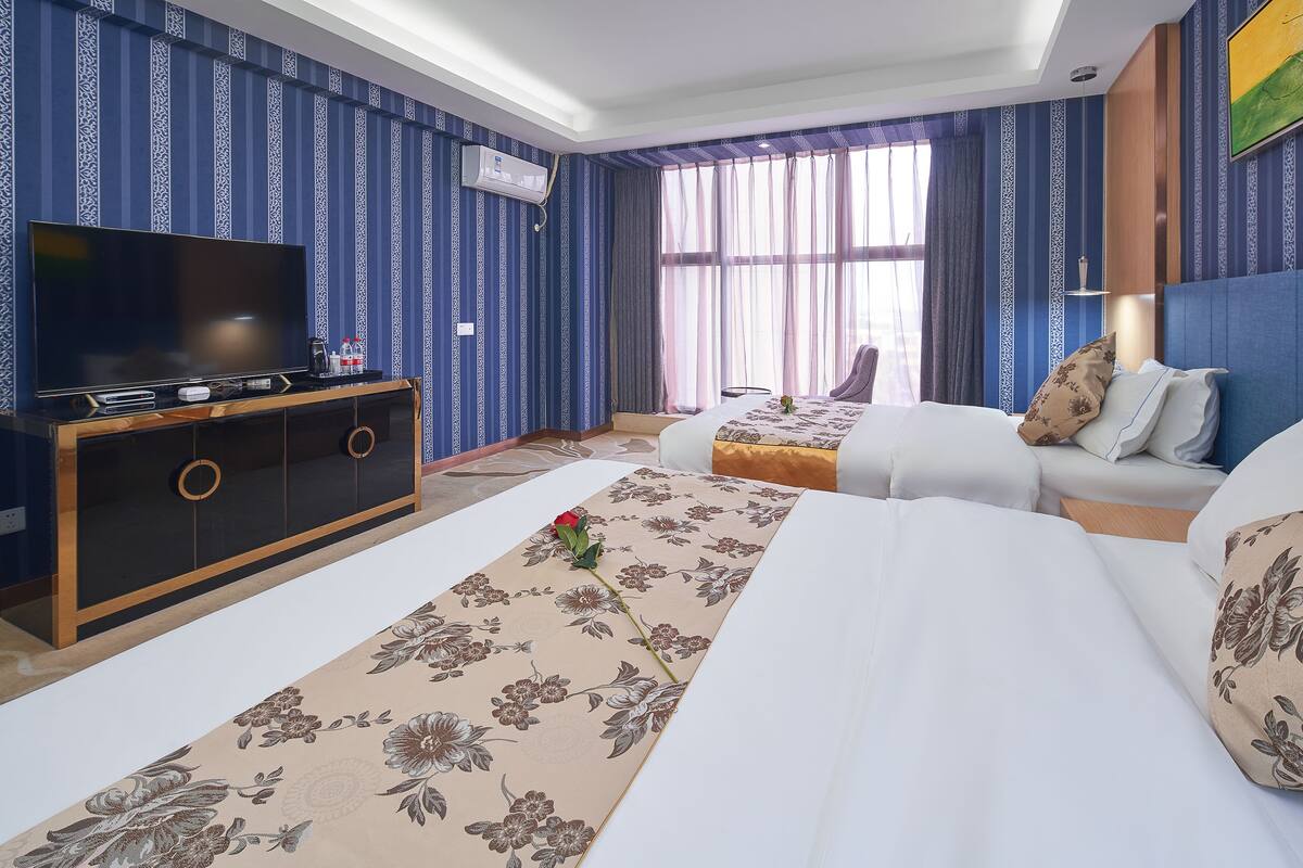 A hotel room with a large flat-screen TV, a sofa, a bed, and a decorative floral runner.