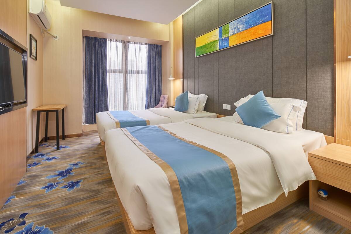 A hotel room with two beds, a television, a small table, and a window with curtains.