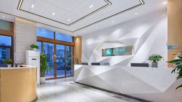 A modern hotel reception area with a geometric design, a reception desk, and a large window offering a city view.