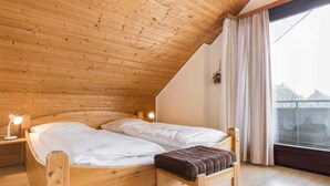 En træseng med to puder og en bænk, en senget lampe og et vindue med gardiner.