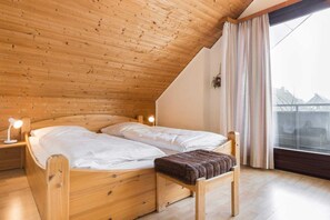 A wooden bed with two pillows and a bench, a bedside lamp, and a window with curtains.