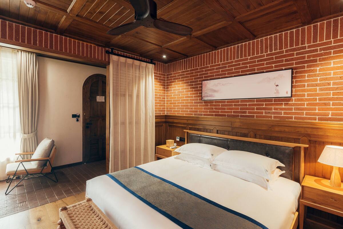 Ein Hotelzimmer mit einem großen Bett, einem Holzkopfstück, einer Ziegelwand und einem Deckenventilator.