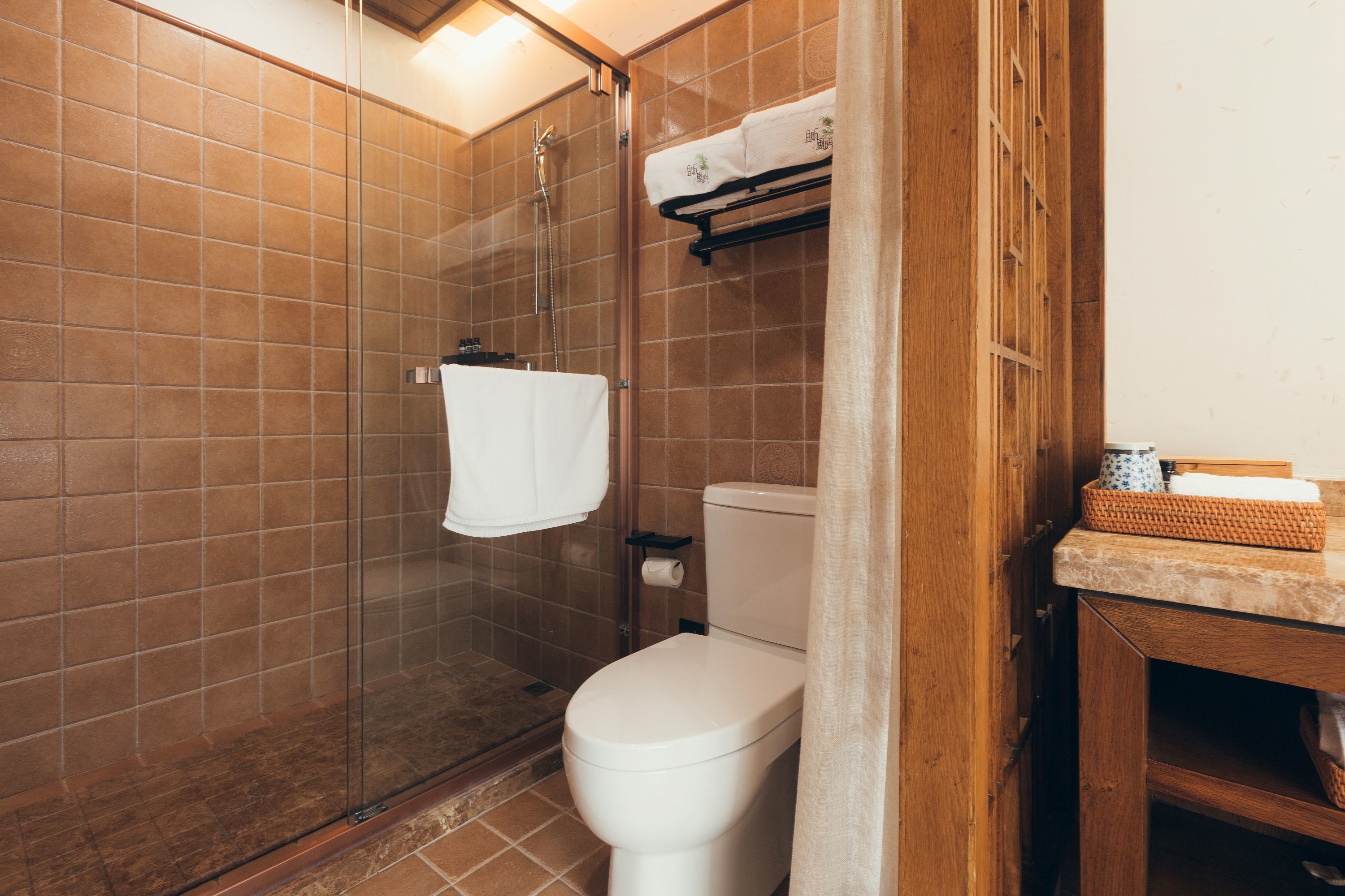 A bathroom with a glass-enclosed shower, a toilet, and a sink area with a towel rack.