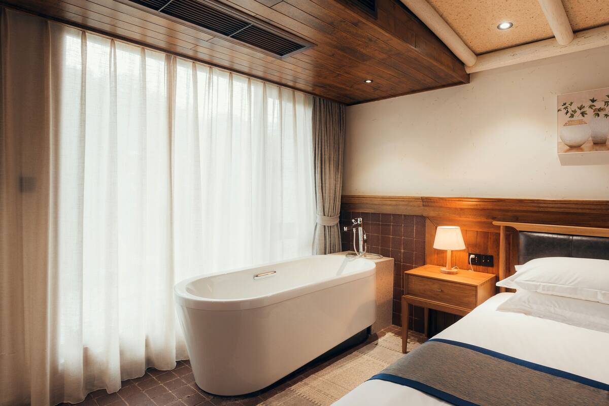 Ein Hotelzimmer mit Badewanne, Nachttisch mit Lampe und einem Bett mit Kissen.