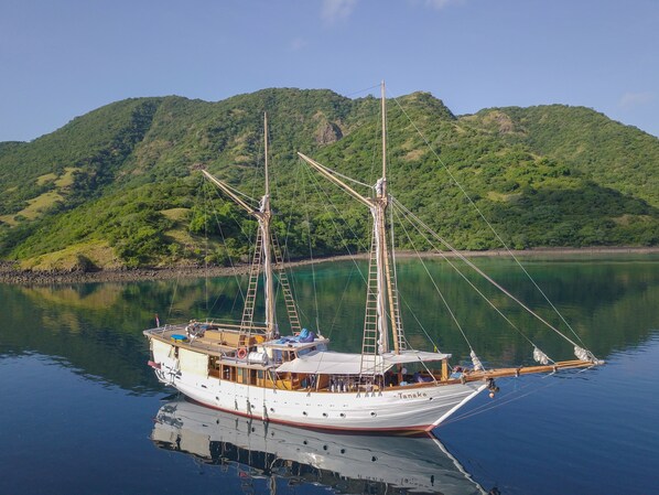 A traditional sailing boat docked at a calm harbor with lush green hills in the background.