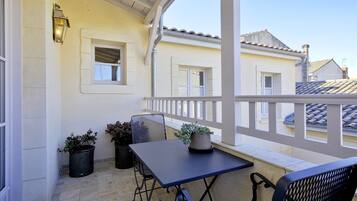 A covered outdoor balcony with a table and chairs, potted plants, and a small window.