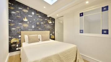 A bedroom with a skylight, a bed with white bedding, a dark patterned wall, and a window with blue decorative panels.