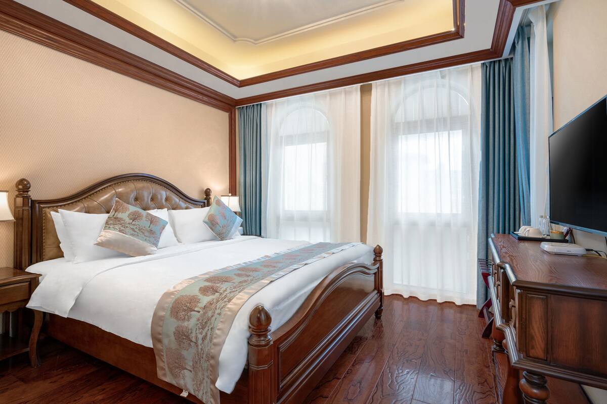 Une chambre spacieuse avec un grand lit, une tête de lit en bois et un téléviseur à écran plat posé sur une commode en bois.