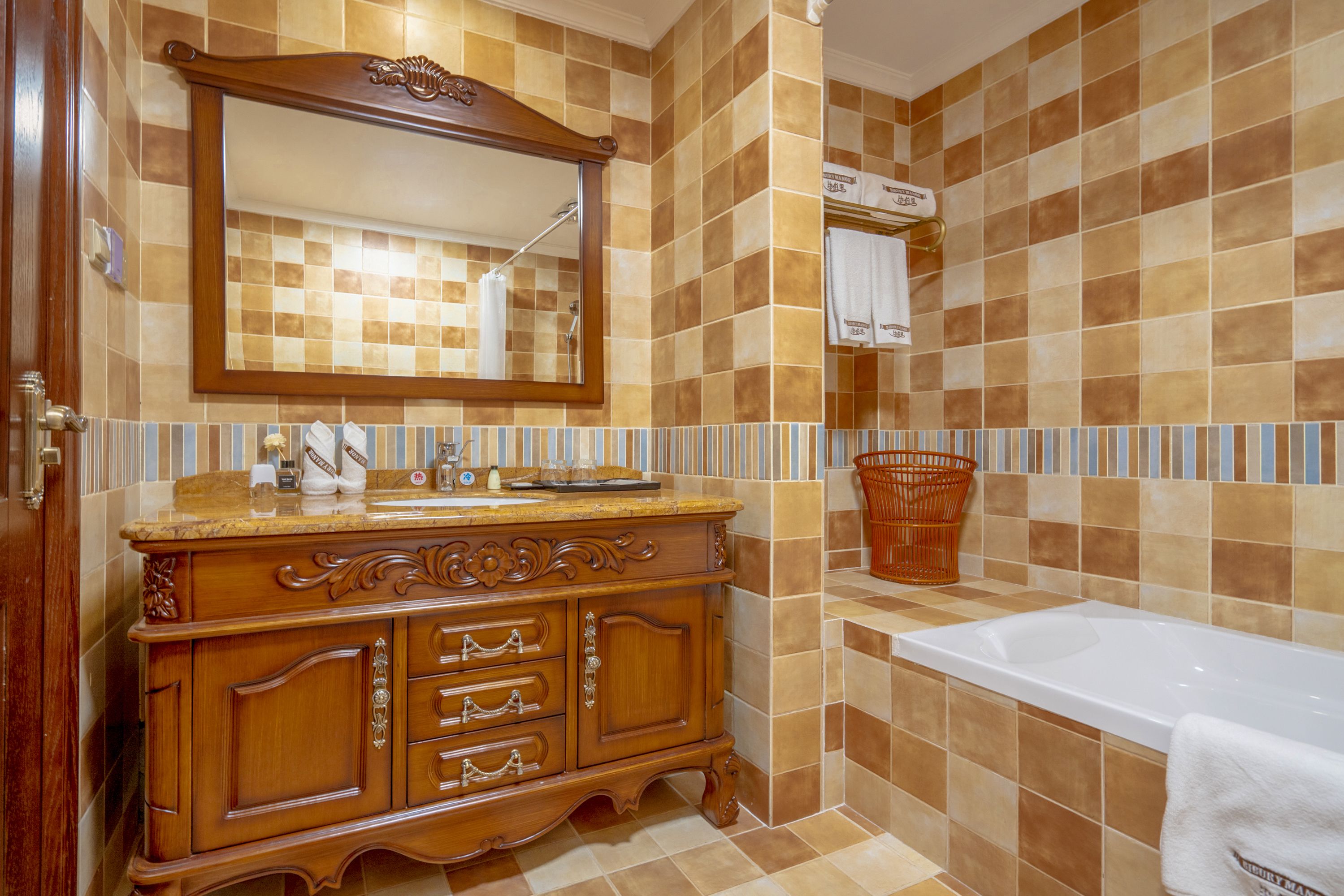A bathroom with a wooden vanity, a large mirror, a bathtub, and a tiled wall.