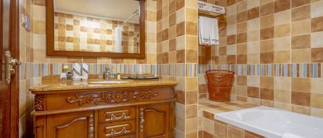 A bathroom with a wooden vanity, a large mirror, a bathtub, and a tiled wall.