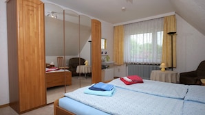 Un dormitorio con cama, armario de madera, escritorio, silla y ventana con cortinas.