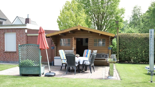 Una cabaña de madera con un patio, mobiliario exterior y un seto al fondo.