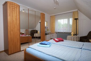 Ein Schlafzimmer mit einem Bett, einem Holzschrank, einem Schreibtisch, einem Stuhl und einem Fenster mit Vorhängen.