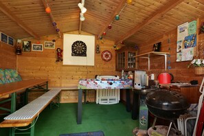 Interior acogedor de una cabaña con dardos, una mesa con mantel, un banco, una parrilla y una alfombra verde.