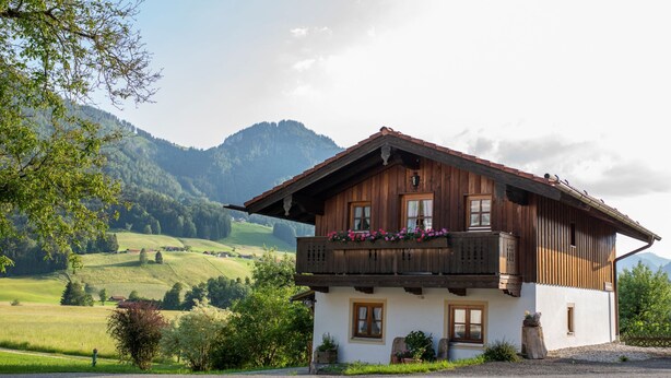 Eine Holzchalet mit Balkon, eingebettet in eine ländliche Landschaft und umgeben von Bergen.
