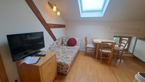 A compact room with a TV, wooden furniture, a skylight, and a small table.
