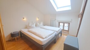 A bedroom with two beds, a skylight, a radiator, and a small table.