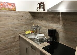 Compact kitchen with a stainless steel sink, electric kettle, and range hood.