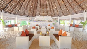 A beachside lounge with white wicker furniture, a bar area, and a thatched roof. - Sandies Bathala (Bathala Island)