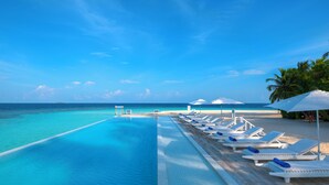 A poolside view with lounge chairs and umbrellas, overlooking a beach and ocean. - Sandies Bathala (Bathala Island)