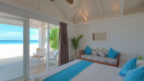 A bedroom with a large bed, a ceiling fan, a view of the beach, and a sliding glass door leading to an outdoor seating area. - Sandies Bathala (Bathala Island)