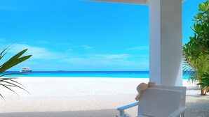 A beachside seating area with a view of the ocean, a boat in the distance, and a tray with a teapot, cups, and cookies. - Sandies Bathala (Bathala Island)