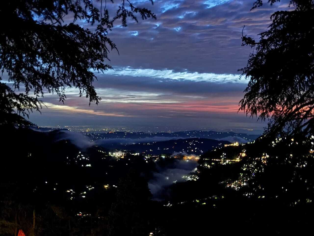 A nighttime cityscape with a view of the city lights and a sunset sky.